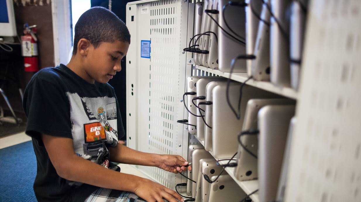 Ein Schüler räumt im Klassenzimmer ein Regal mit Chromebooks auf.