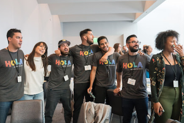 Five Googlers stand and sing with their arms around each other while two other Googlers stand next to them smiling