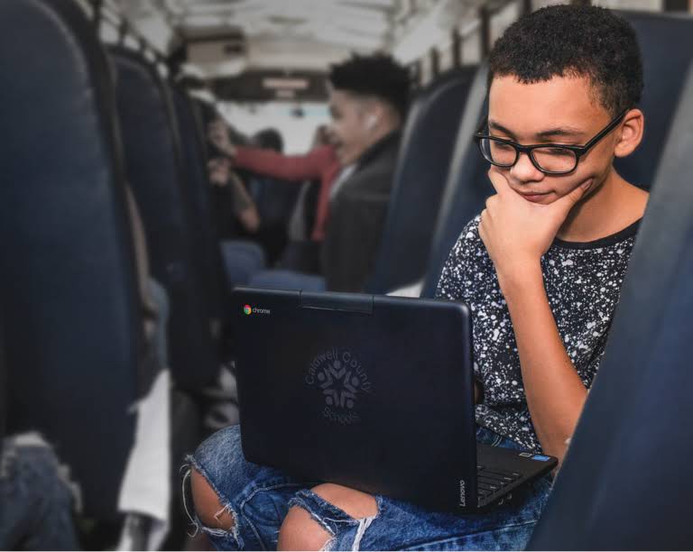 เด็กนักเรียนใส่แว่นกำลังตั้งใจดูอุปกรณ์ Chromebook บนรถโรงเรียน