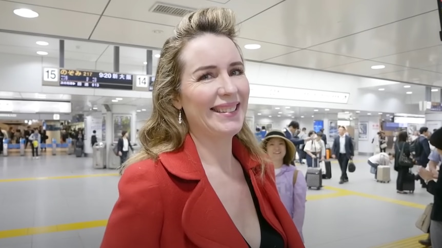 a woman with a red blazer smiles inside a train station