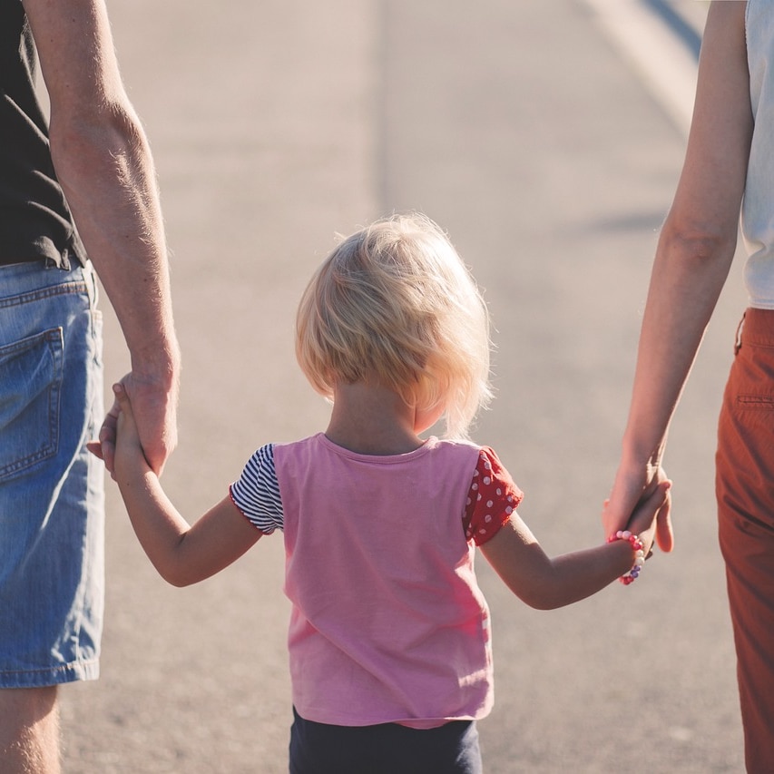 Young child holds hands with parents