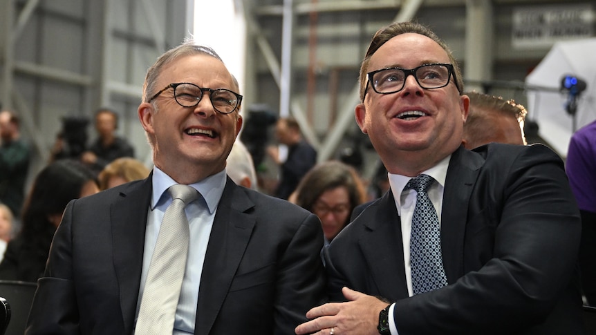 Alan Joyce touches Anthony Albanese as they sit together at an unveiling in a Qantas facility. Adam Goodes is also pictured