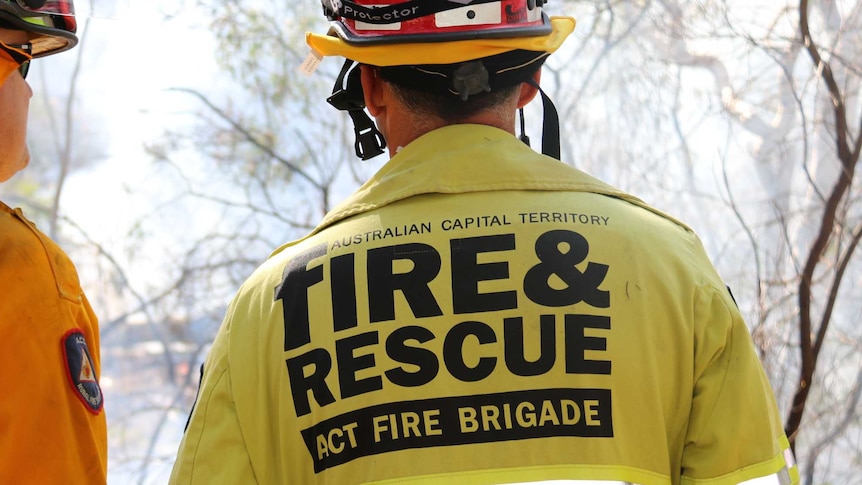 Two firefighters, one from ACT Fire and Rescue and one from ACT Rural Fire Service look out at a smouldering fire.