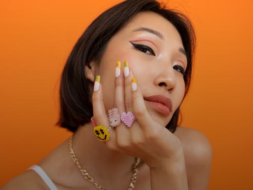 A woman with dark hair and unique jewelry in front of an orange background.