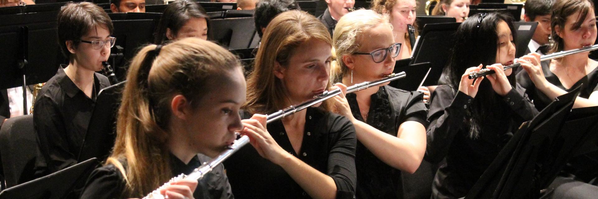 Students in the band playing on their flutes during a concert.