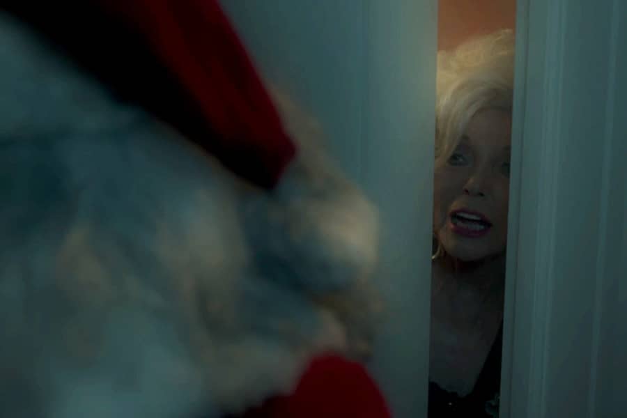 the older woman opens the door a crack to speak to a Santa outside