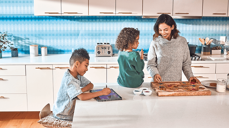 Moeder staat en twee kinderen zitten samen in een keuken.